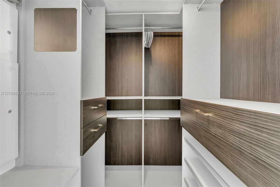 Custom closet system featuring wood-finish cabinetry, built-in shelving, integrated hanging rods, and drawers with metallic hardware