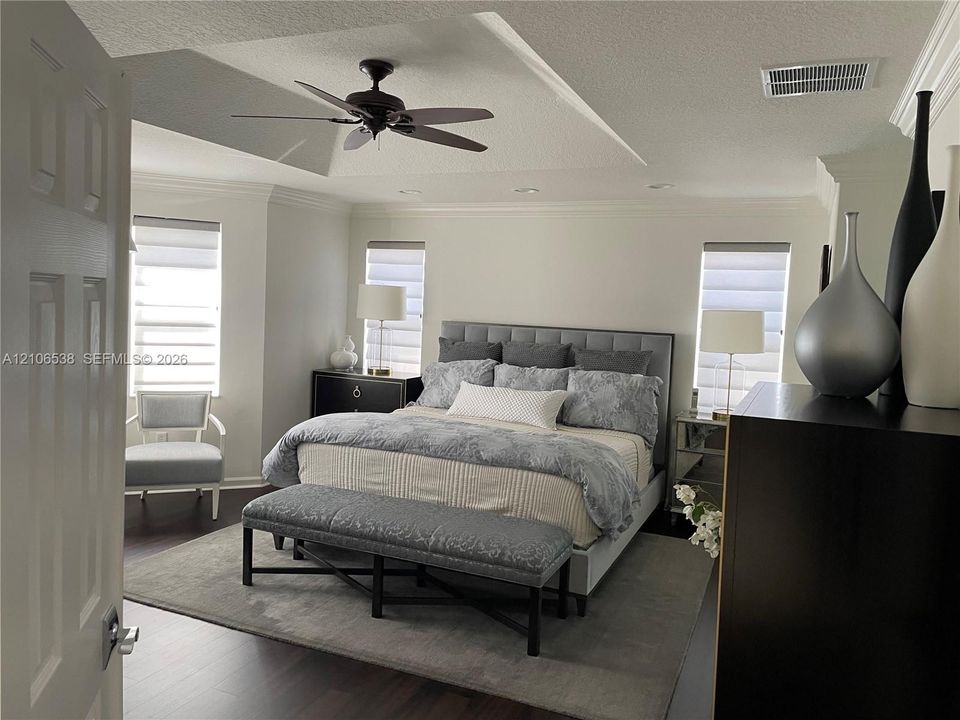 Tray ceiling with integrated recessed lighting, dark wood-finish flooring, bay window configuration, and an overhead ceiling fan