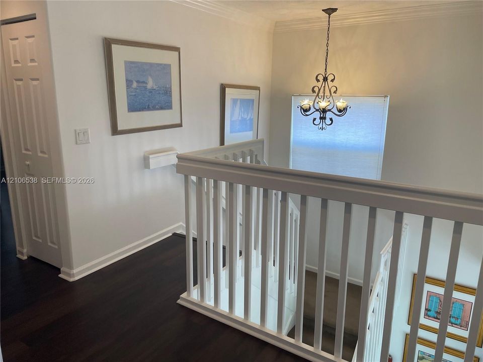 Stairwell featuring white-painted wood balusters, dark wood-finish flooring, and an ornamental multi-light chandelier
