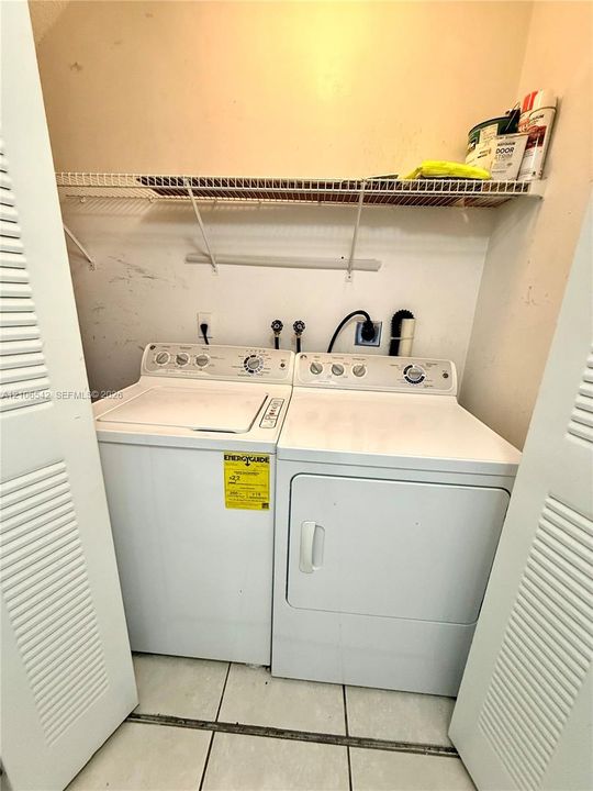 Dedicated laundry area featuring dual louvered closet doors, a metal wire shelving unit, and tile flooring