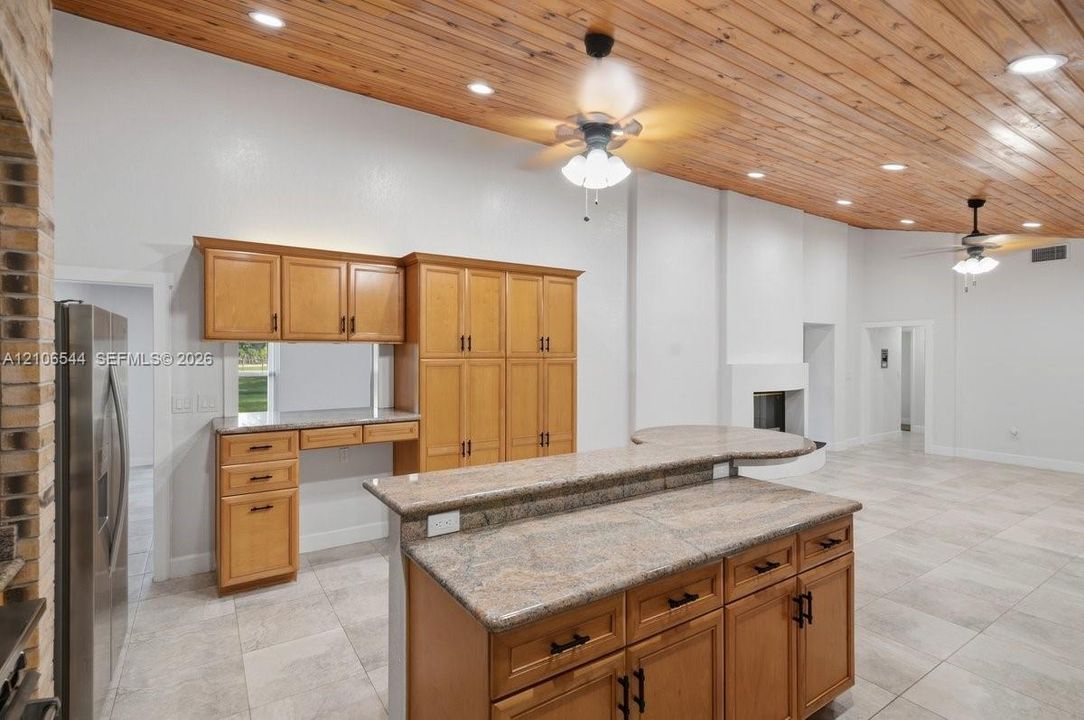 Vaulted wood-plank ceiling, stone-surfaced kitchen island with breakfast bar, built-in cabinetry, ceramic tile flooring, and integrated fireplace