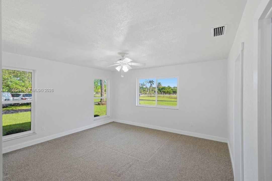 Interior space featuring neutral-toned carpeting, three sliding windows, and a white ceiling fan with integrated lighting