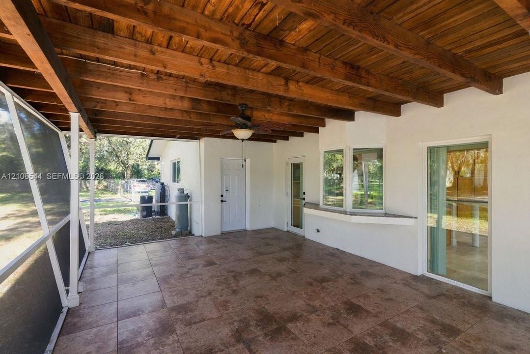 Covered patio featuring exposed wood beam ceiling, tile flooring, screen enclosure, and ceiling-mounted light fixture