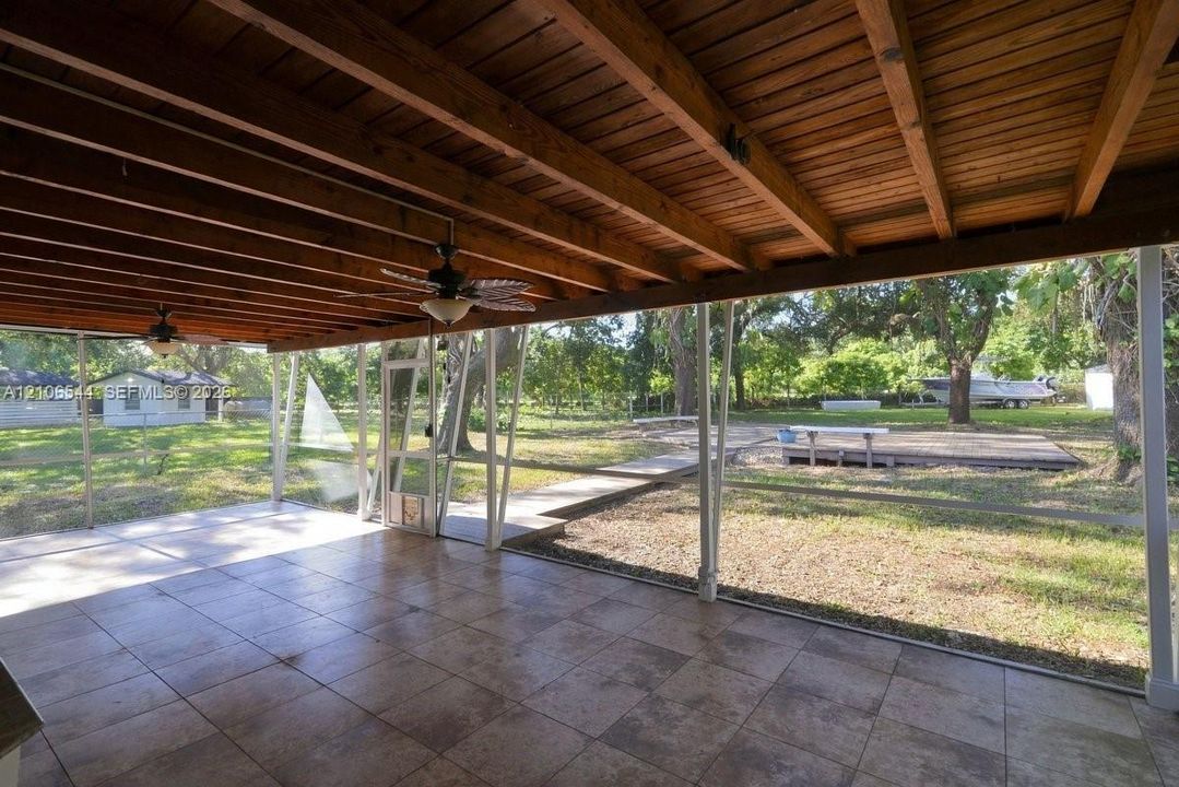 Screened-in patio featuring tile flooring, exposed wood-beam ceiling, ceiling fans, and structural metal support columns