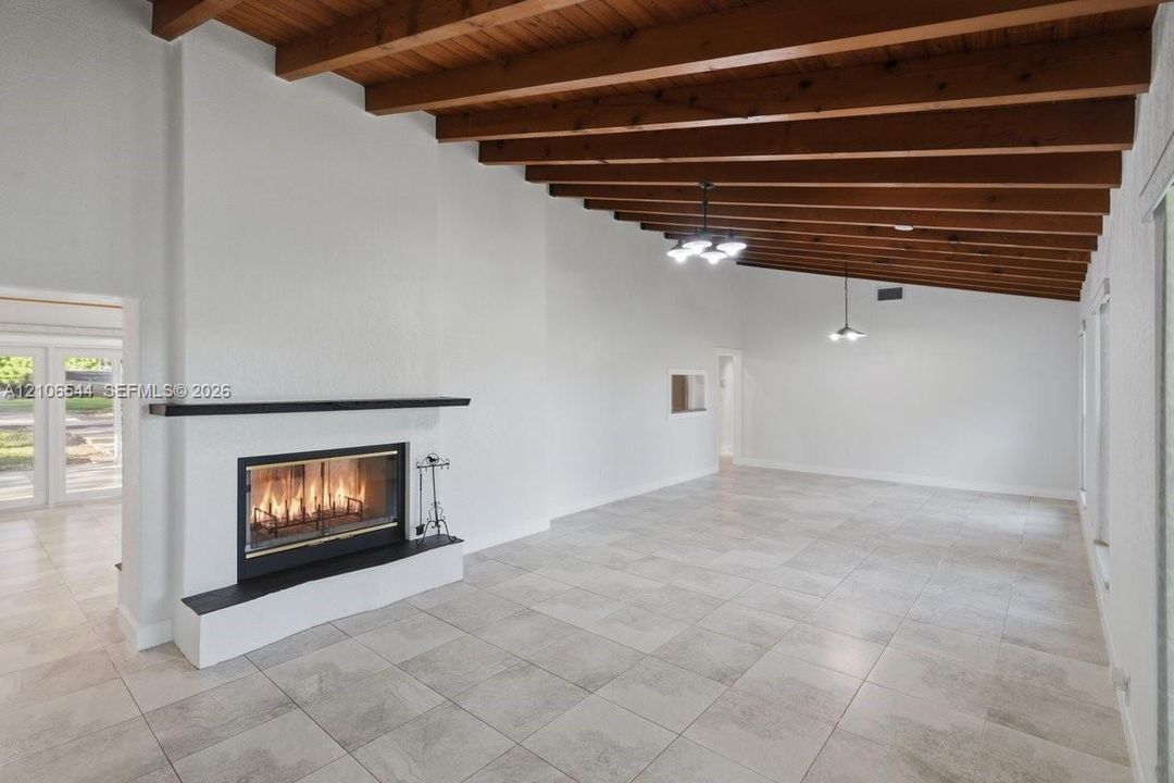 Exposed wood beam ceiling, large-format tile flooring, built-in fireplace with a sleek mantel, and minimalist pendant lighting