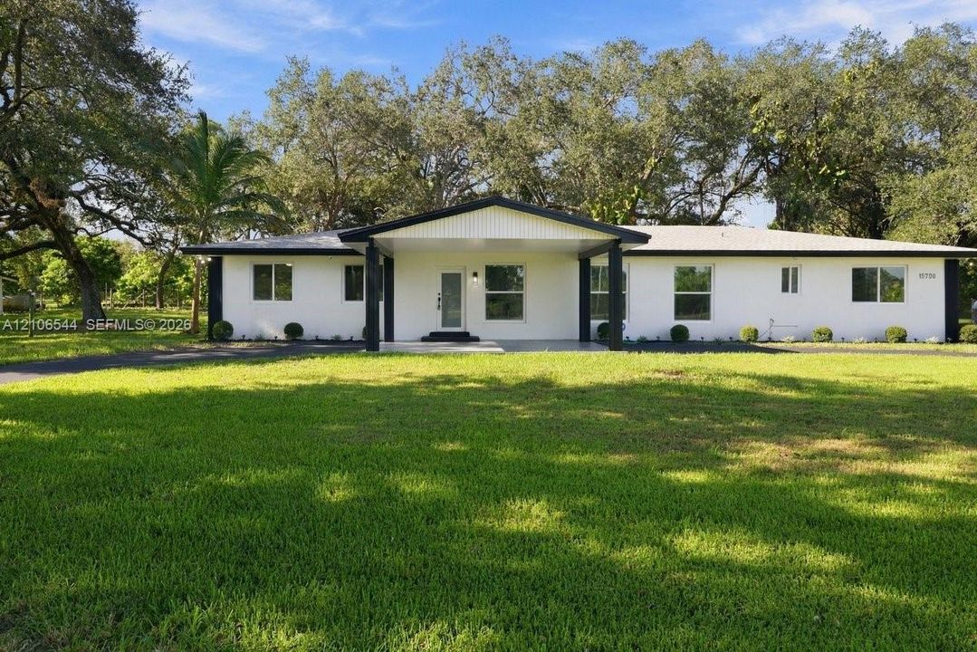 Single-story residence featuring a painted masonry exterior, a covered entryway with structural columns, and an expansive front lawn with mature oak trees
