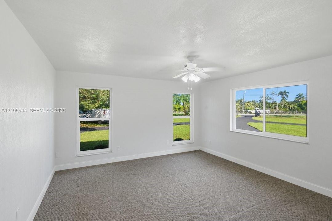 Neutral-toned wall-to-wall carpeting, three sliding-style windows, and a ceiling-mounted light fixture with a fan