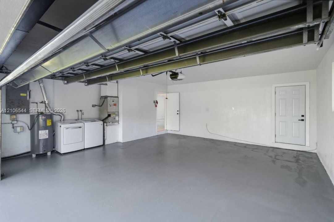 Garage interior featuring painted flooring, overhead door mechanism, integrated water heater, and a dedicated utility area with built-in laundry hookups