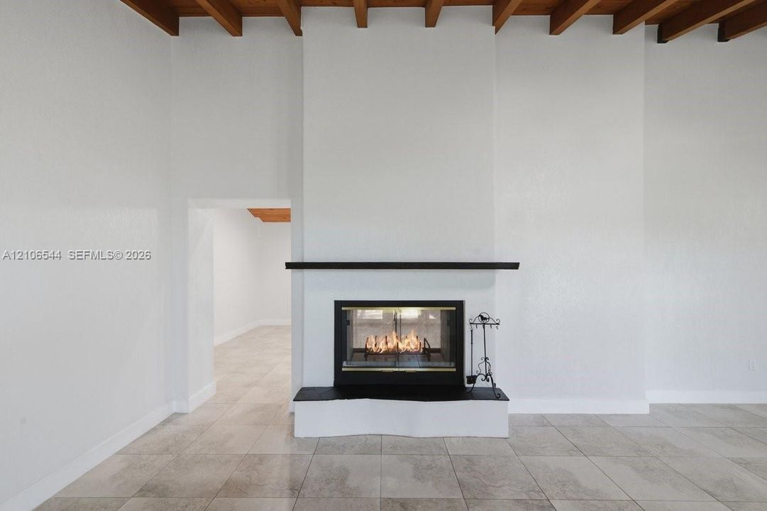 Fireplace featuring a black hearth, mantle, and glass-enclosed insert, set against a floor-to-ceiling surround with exposed wood ceiling beams and large-format tile flooring