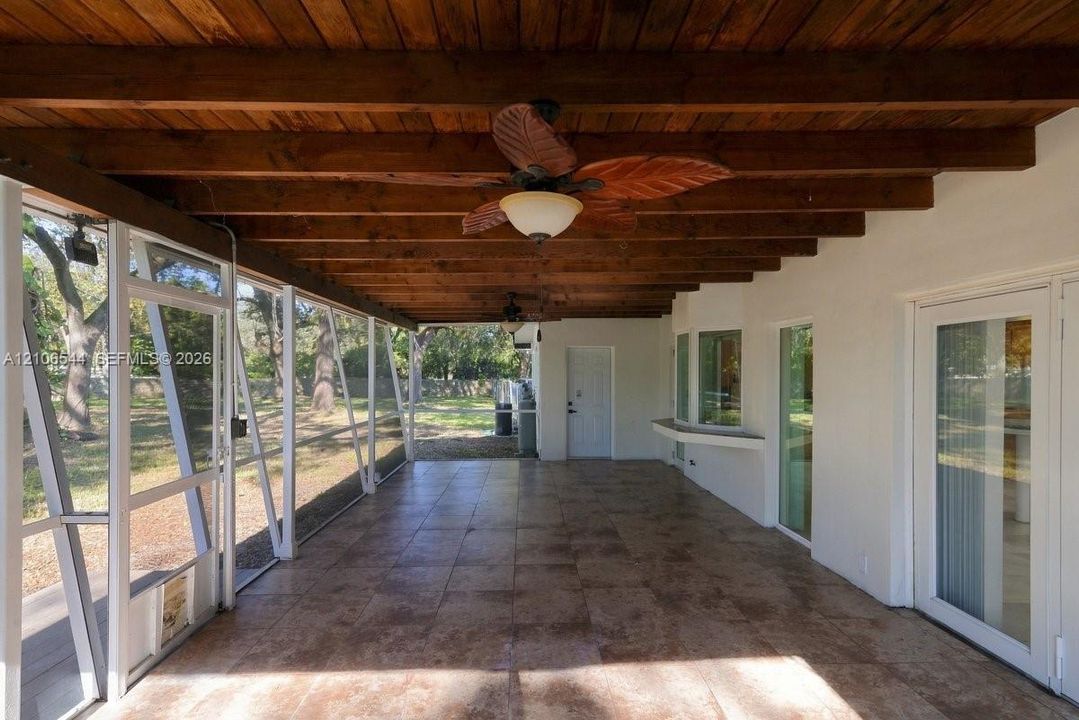 Screened-in patio featuring an exposed timber beam ceiling, tile flooring, built-in wall shelf, and ceiling-mounted fans