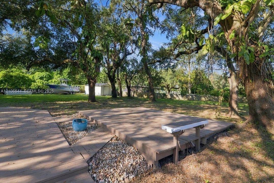 Rear grounds featuring an elevated composite deck, stone-accented hardscaping, and mature canopy trees