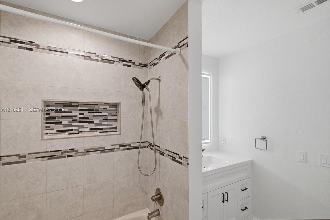 Tiled shower featuring a decorative mosaic inlay, handheld shower head, white vanity with cabinetry, and an integrated LED mirror