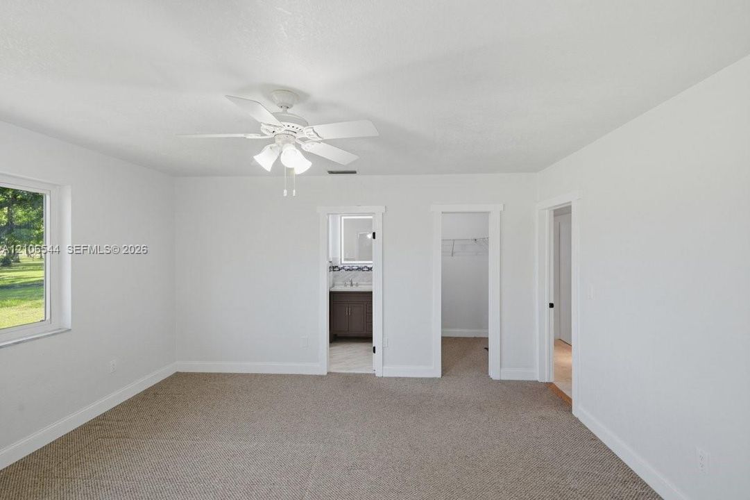 Neutral interior featuring wall-to-wall carpeting, a white ceiling fan with integrated lighting, and multiple doorways
