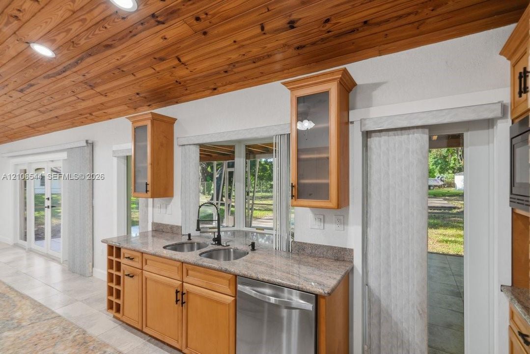Kitchen featuring a vaulted wood-plank ceiling, recessed lighting, stone-finish countertops, stainless steel dual-basin sink with a matte black faucet, and natural wood cabinetry with glass-panel doors