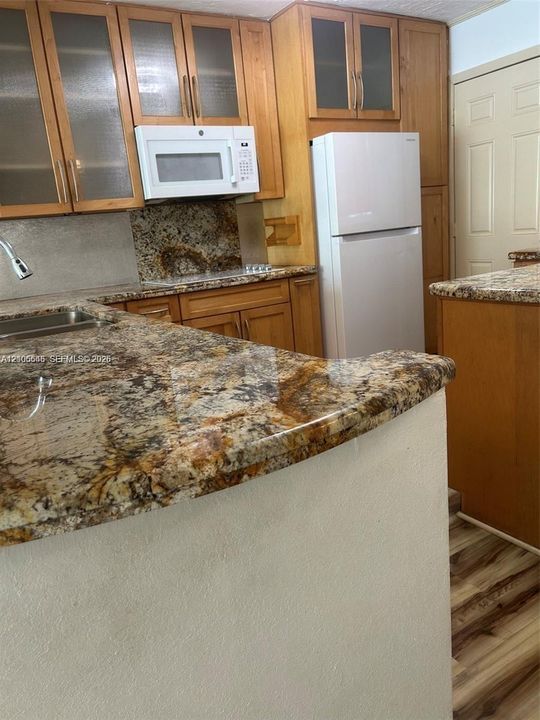 Kitchen featuring stone countertops, wood-finish cabinetry with glass-panel upper doors, built-in microwave, and wood-finish flooring