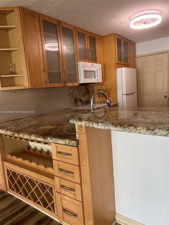 Kitchen featuring wood cabinetry with glass-panel upper doors, stone-surface countertops, built-in wine storage, and wood-finish flooring