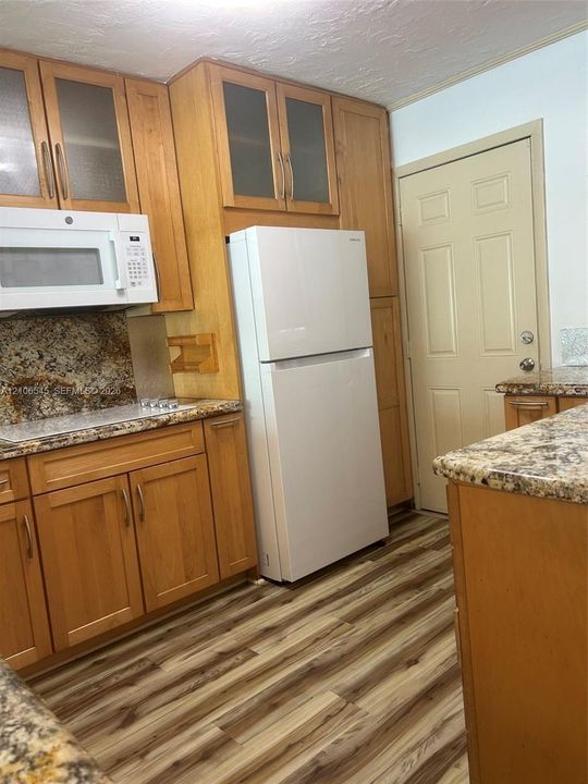 Kitchen featuring wood cabinetry with glass-panel upper doors, stone-finish countertops, and wood-finish flooring