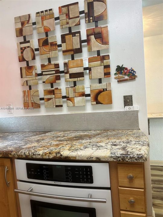 Stone-patterned countertop with a coordinating neutral backsplash, paired with light-finish wooden cabinetry and a built-in white oven