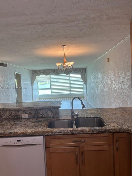Kitchen featuring stone-finish countertops, stainless steel double-basin sink, high-arc faucet, and wood-finish cabinetry, complemented by a multi-arm chandelier