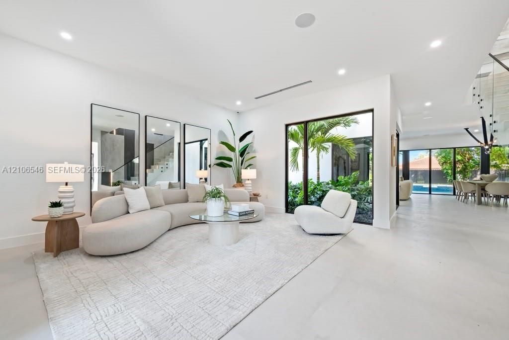 Living area featuring large-format tile flooring, floor-to-ceiling mirrors, recessed lighting, and expansive glass walls opening to an interior garden
