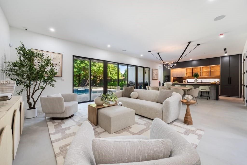 Open-concept living space featuring large-format tile flooring, recessed lighting, multi-panel sliding glass doors, and a modern kitchen with dark cabinetry and illuminated shelving