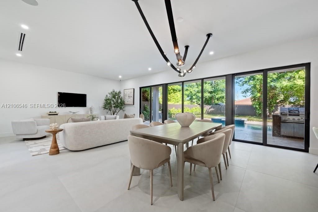Large-format tile flooring, recessed ceiling lighting, contemporary multi-arm chandelier, and floor-to-ceiling sliding glass doors opening to the outdoor pool area