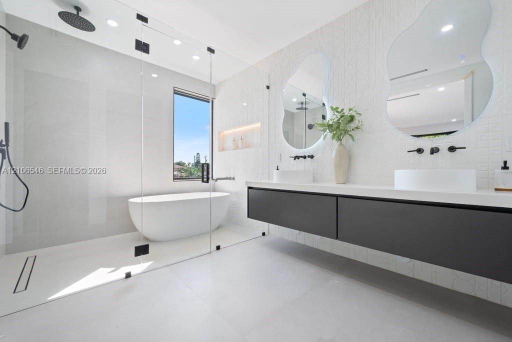 Modern bathroom featuring a glass-enclosed wet room with a freestanding soaking tub, floating double-drawer vanity, dual vessel sinks, and matte black wall-mounted fixtures