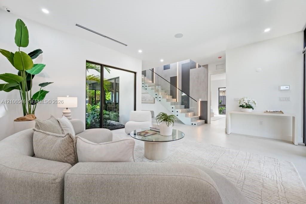 Open-concept interior featuring large-format flooring, recessed lighting, a glass-railing staircase with integrated vertical lighting, and floor-to-ceiling windows