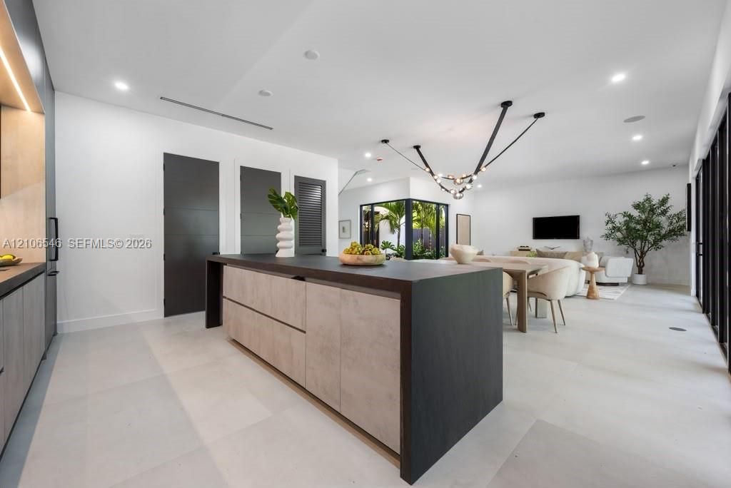Open-concept living space featuring a central kitchen island with wood-finish cabinetry and a dark countertop, large-format tile flooring, recessed lighting, and a multi-arm modern light fixture