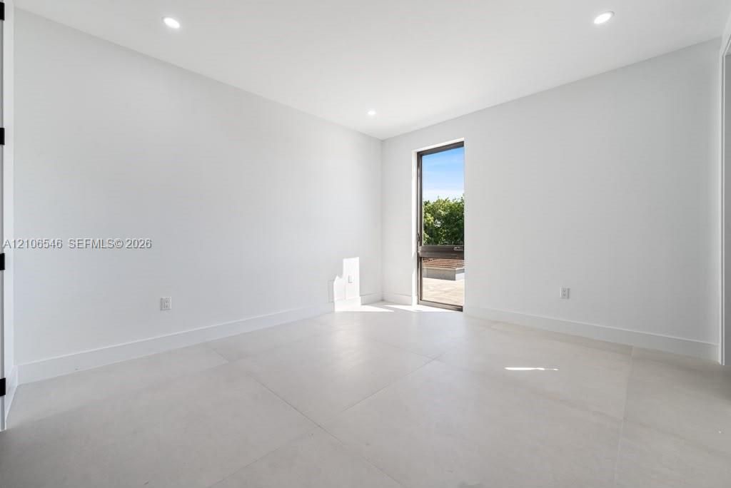 Minimalist room featuring large-format tile flooring, recessed ceiling lighting, and a floor-to-ceiling glass panel door