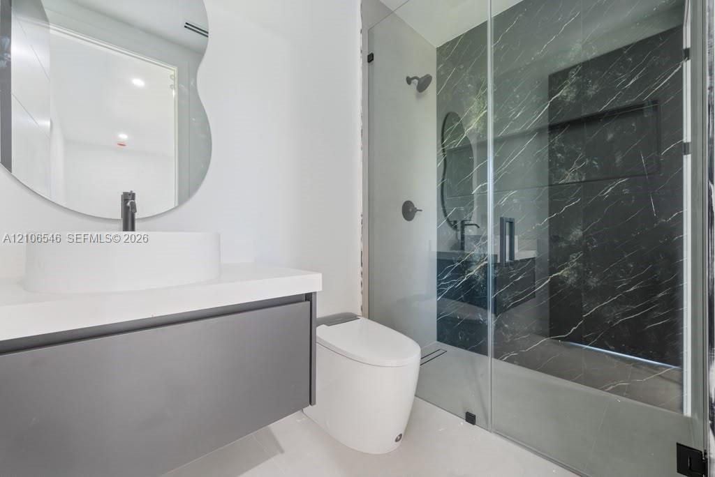 Floating vanity with a white vessel sink, dark stone-finish shower surround, glass shower enclosure, and organic-shaped wall mirror