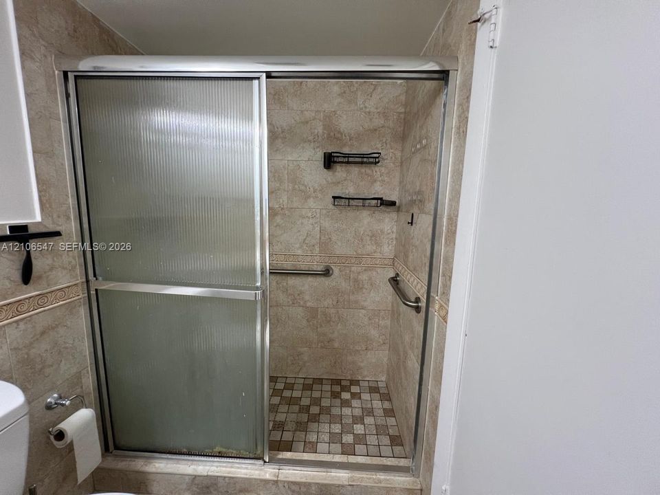 Walk-in shower enclosure featuring ribbed sliding glass doors, neutral-toned tiled walls with decorative border accents, mosaic tile flooring, and integrated metal grab bars