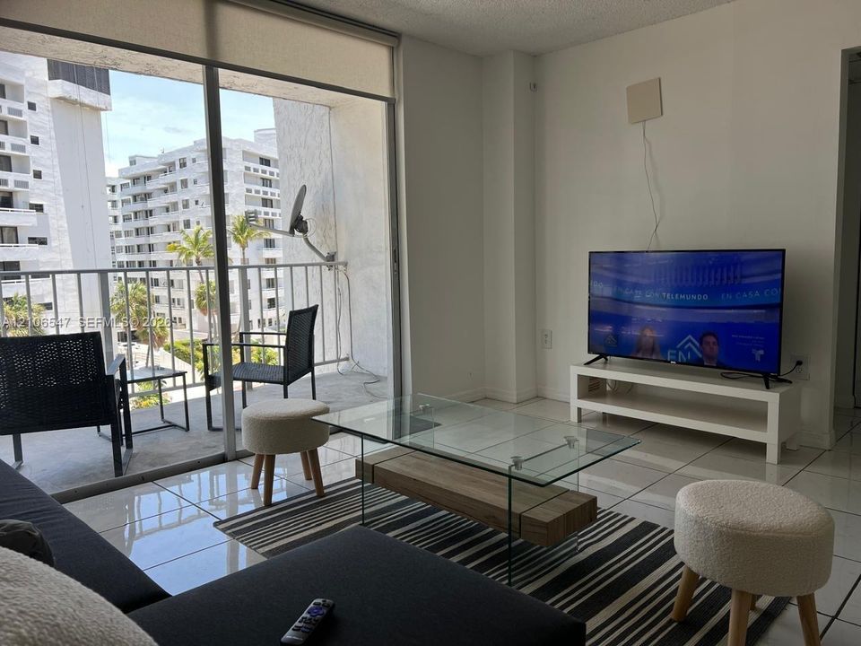 Floor-to-ceiling sliding glass doors, white tiled flooring, and a private balcony with metal railing