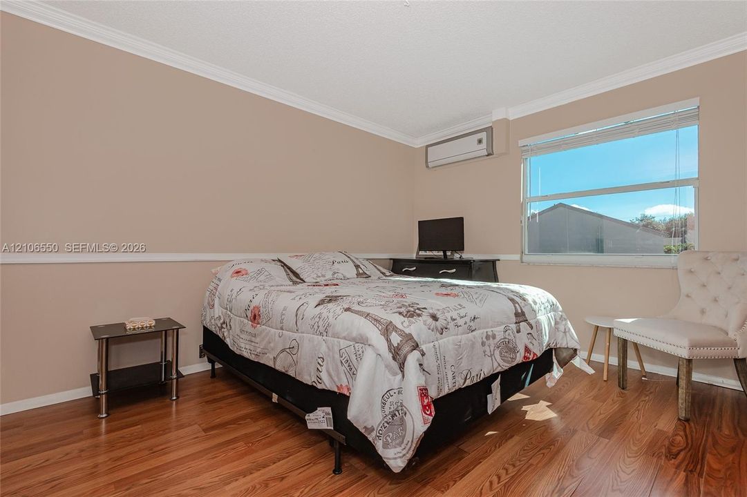 Bedroom featuring wood-finish flooring, chair rail molding, and large window with horizontal blinds