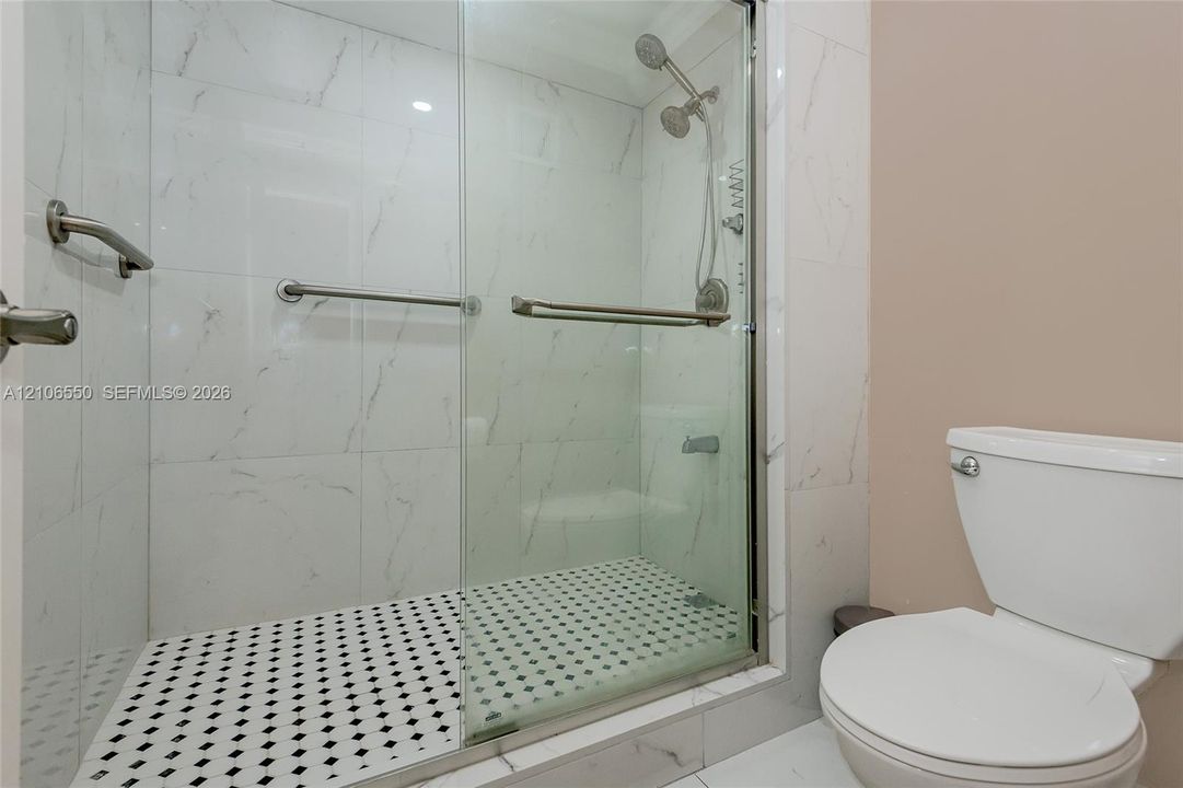 Primary Bathroom. Walk-in shower featuring large-format stone-look wall tiling, a mosaic tile floor, glass sliding doors, and chrome fixtures