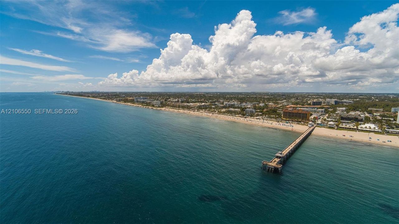 Aerial perspective of coastal landscape featuring an expansive sandy shoreline and extended deep-water pier