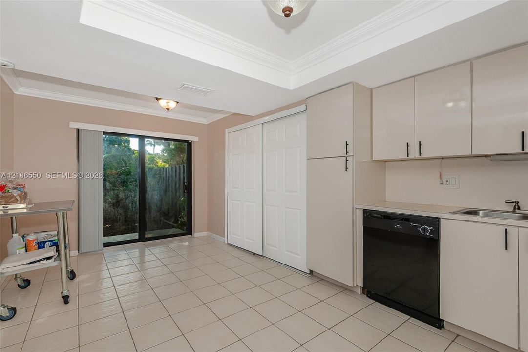 Kitchen featuring gloss-finish cabinetry, built-in dishwasher, integrated sink, tile flooring, and sliding glass doors with tray ceiling detail. large eat-in kitchen with breakfast nook with plenty of storage