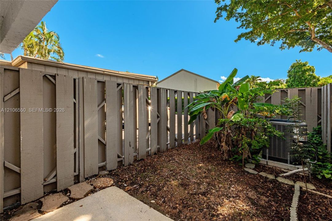 Private outdoor space featuring vertical wood-slat privacy fencing, concrete patio slab, mulch ground cover, and mature tropical greenery