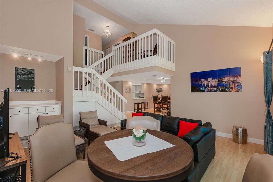 Vaulted ceiling, open mezzanine with white balustrade, wood-finish flooring, and built-in cabinetry