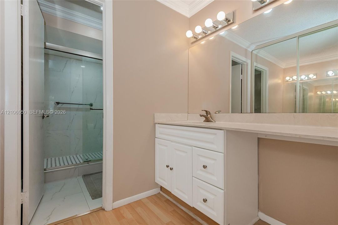 Primary Bathroom vanity featuring a white cabinet base, stone-look countertop, integrated sink, and full-width wall mirror with attached multi-bulb lighting