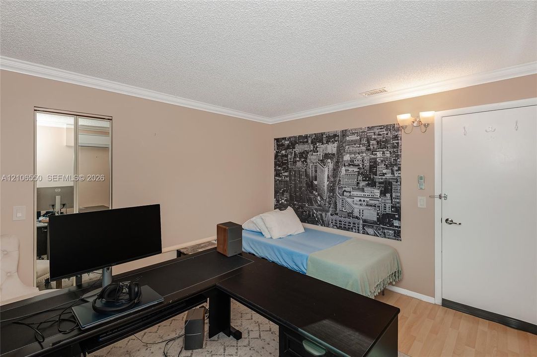 Room featuring wood-finish flooring, crown molding, dual-panel closet doors with mirror inserts, and wall-mounted light fixture