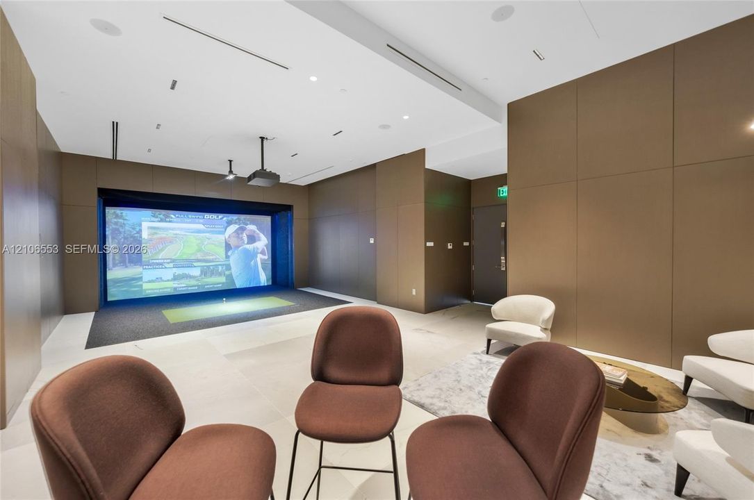 Golf simulator room featuring large-format tile flooring, integrated ceiling-mounted speakers, recessed linear lighting, and wood-paneled walls