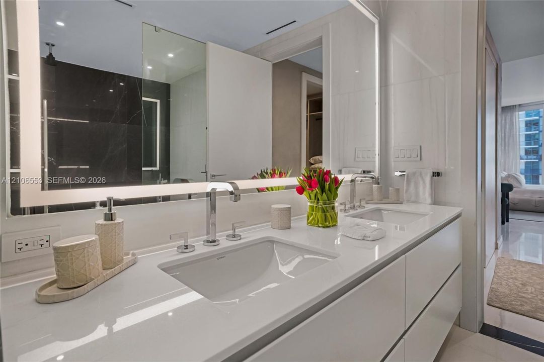 Floating double vanity featuring a seamless countertop with integrated dual sinks, chrome widespread faucets, and a large wall-mounted mirror with integrated perimeter lighting