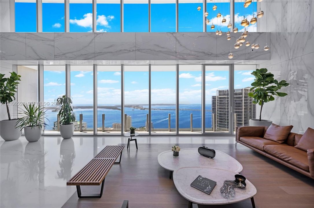 Double-height floor-to-ceiling windows, stone-clad accent wall, polished stone flooring, wood-finish flooring, and multi-tiered glass pendant lighting