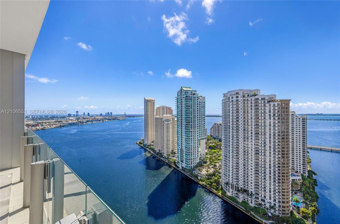 Private balcony featuring glass panel railing and tile flooring, capturing coastal waterway scenery and urban skyline