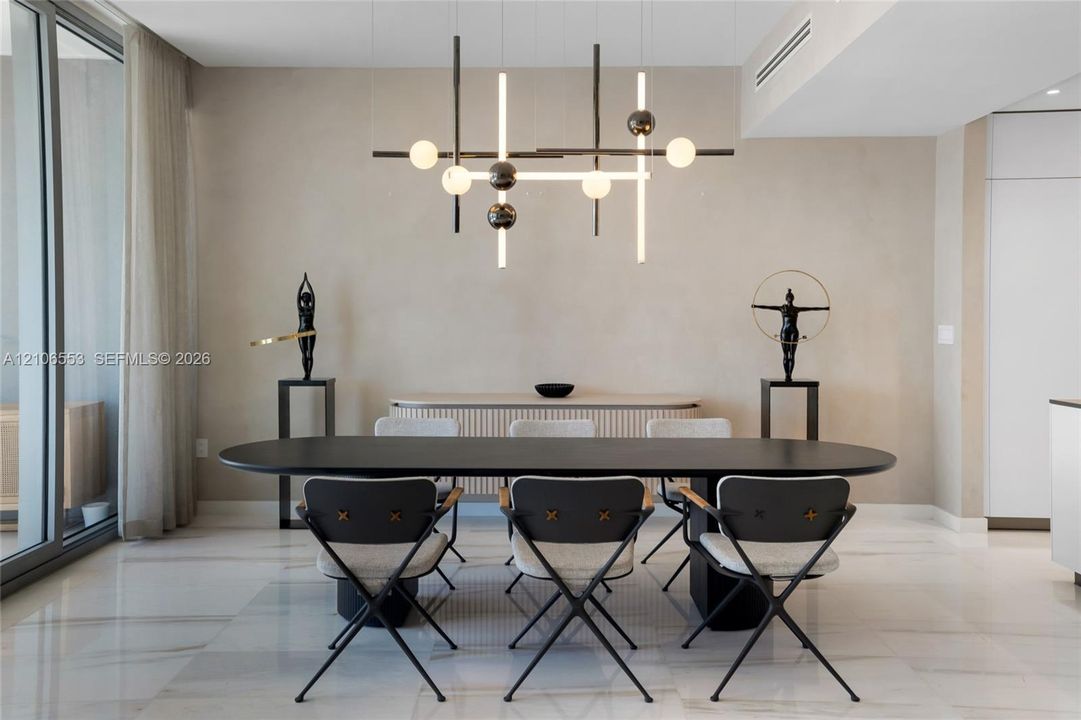 Modern living space featuring large-format stone flooring, floor-to-ceiling glass sliding doors, textured wall finishes, and a linear geometric multi-light chandelier