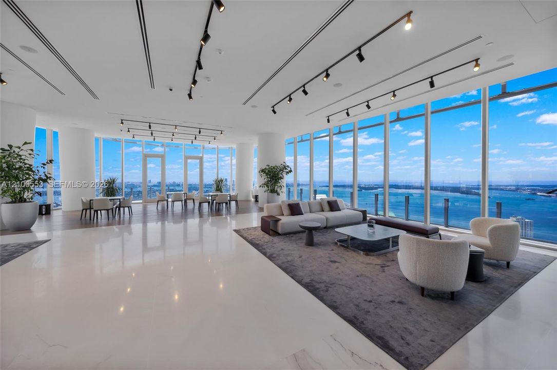 Expansive open-concept floor plan featuring floor-to-ceiling glass walls, polished stone flooring, industrial-style track lighting, and structural columns