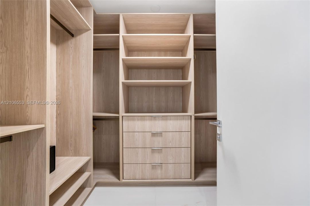 Custom closet organization system featuring light wood-finish cabinetry, built-in shelving, integrated hanging rods, and a four-drawer dresser unit with metallic pulls