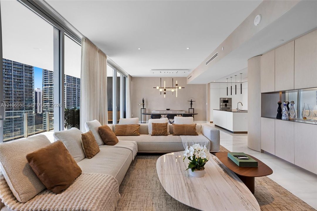 Floor-to-ceiling glass windows, expansive stone flooring, integrated cabinetry, modern linear light fixtures, and white waterfall-edge kitchen island