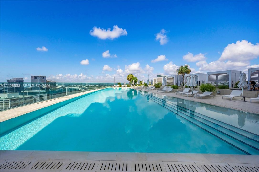Rooftop infinity-edge pool featuring a glass perimeter railing, submerged tiered steps, and stone-tiled decking